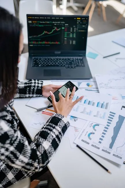 Person using smartphone for stock market analysis at home office.
